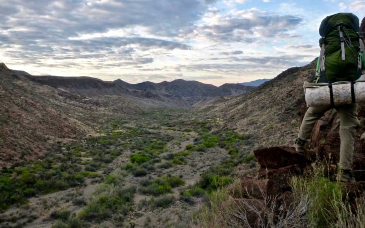 an outward bound student wearing a backpack looks over a desert valley from a high vantage point